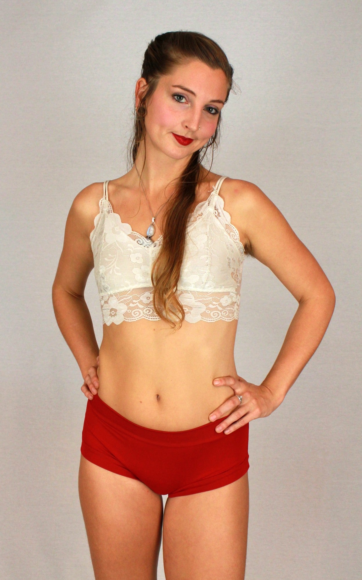 Woman wearing a white lace bralette and red shorts against a plain background